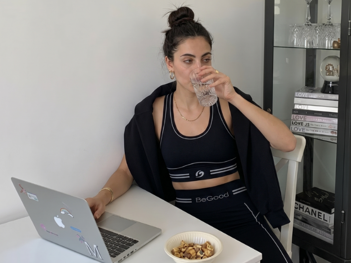 Ragazza in smart working al pc da casa, indossa leggings anticellulite BeGood e beve acqua mentre lavora alla scrivania.